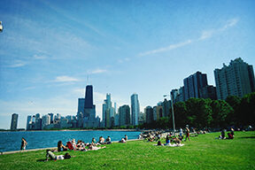 People relaxing by Lake Michigan in summer, city skyline in background.