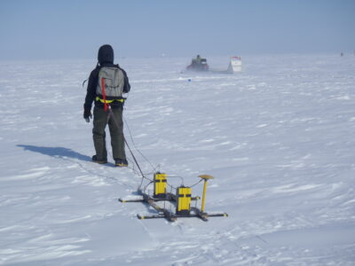 Man walks through snow with research device.